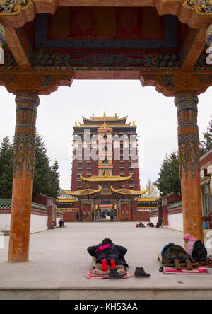 Il Tibetano pellegrini pregano e prostrarsi di fronte Hezuo monastero e la sua torre milarepa, provincia di Gansu, Hezuo, Cina Foto Stock