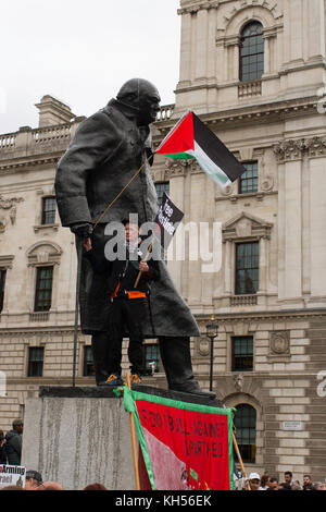 Un protestor sorge su Churchill's plinto di onde e la bandiera palestinese, la piazza del Parlamento, Londra. Foto Stock