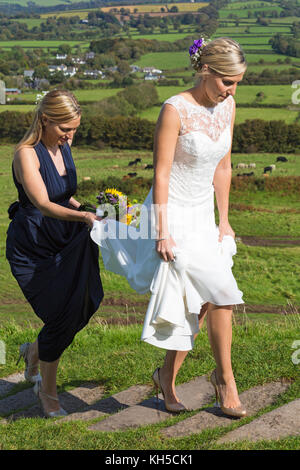 Sposa e damigella fasi ascendenti alla chiesa di San Michele de Rupe, San Michele della roccia, a Brentor, Parco Nazionale di Dartmoor, Devon, Regno Unito nel settembre Foto Stock