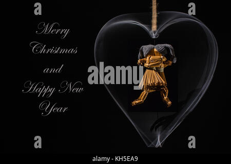 Auguri di Natale con bambole di paglia danzanti in un cuore di metallo rotante e con il testo: Buon Natale e felice anno nuovo Foto Stock