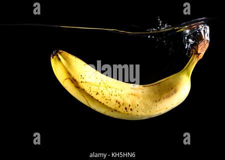 Close up di una banana caduta in acqua isolate su uno sfondo nero Foto Stock