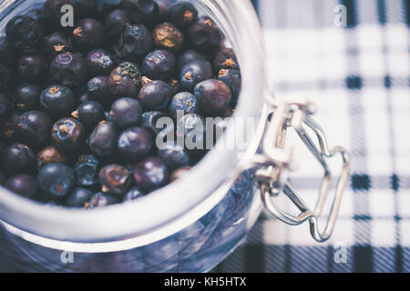 Il gin ingrediente: bacche di ginepro in un barattolo di vetro sul blu e bianco di tartan Foto Stock