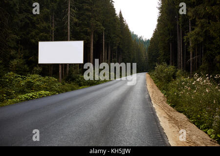 Tabellone vuoto segno da vuoto autostrada attraverso la foresta montagne paesaggio. annuncio pannello sulla strada. strada forestale con tabellone bianco per il vostro testo. mock up Foto Stock