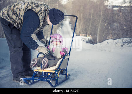 Active senior adulto uomo con la sua nipote slittino in winter park in caso di neve durante le vacanze invernali Foto Stock