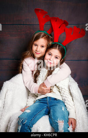 Due piccolo felice ragazze sorridenti abbracciando .concetto di Natale. Sorridente funny sorelle di corna di cervo in studio. Foto Stock