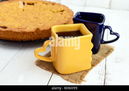 Due belle coppe (blu scuro e giallo) con caffè, tè e pane appena sfornato dolci fatti in casa con confettura di albicocca. Foto Stock
