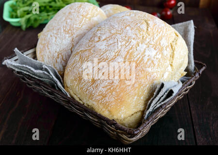 Ciabatta - Pane appena sfornato italiano di pane bianco nel cesto su legno scuro dello sfondo. per la preparazione di panini. Foto Stock