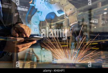 Imprenditore è usato Smart Phone Control automatizza wireless robot di saldatura. È industrial4.0 concetto con doppia esposizione Foto Stock