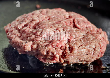 Un hamburger patty la frittura su una griglia in ghisa Foto Stock