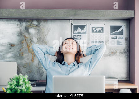 Asian creative designer sollevare il braccio e il resto in corrispondenza della parte posteriore della testa e chiudere gli occhi di fronte a computer laptop sulla scrivania,relax dal duro lavoro in ufficio. Foto Stock