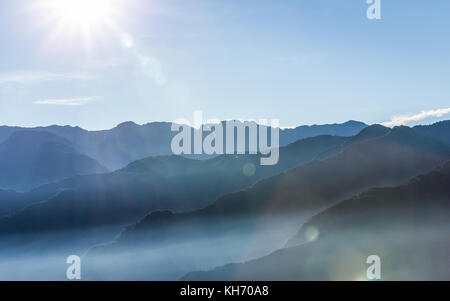 Fumoso montagne blu di Zhushan all'interno Alishan Recreation Area di Taiwan coperti dalla nebbia durante il sorgere del sole al mattino con un luminoso cielo d'inverno. Foto Stock