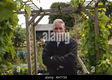 Ritratto di senior uomo in piedi con le braccia incrociate in giardino Foto Stock