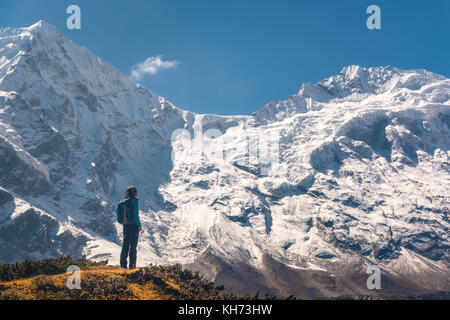 In piedi giovane donna sulla collina e guardando sulla stupefacente montagna himalayana. Paesaggio con traveler, alte rocce con vette innevate, cielo blu in autunno Foto Stock