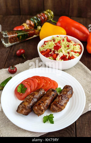 Succosa rotoli grigliate di carni macinate avvolto in pancetta con pomodoro fresco e una luce insalata di cavolo cinese e peperone. Foto Stock