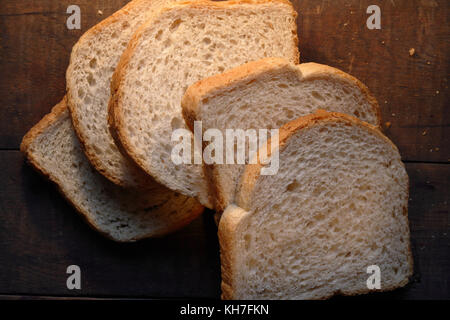 Alcuni pezzi di fettine di pane bianco giacente su scuro dello sfondo in legno Foto Stock