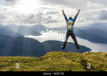 L'uomo raggiungendo il culmine e saltando di gioia. splendida vista alle montagne costiere e fiordi. hellandsnuten, sandsfjord, Norvegia. Foto Stock