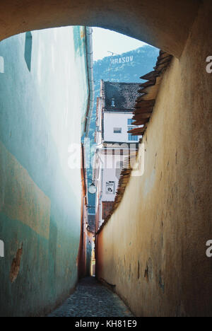 Una stretta viuzza strada sforii, una tra le più strette in Europa, ald vintage pareti e una vista di una montagna con un segno di brasov sulla città. Foto Stock