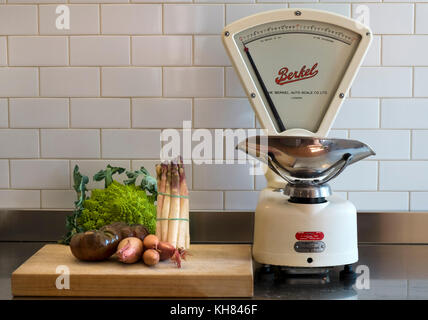 Alcune verdure a scelta in attesa su di un tagliere su un acciaio inossidabile cucina superficie di lavoro a fianco di un set di classic vintage grocers bilance di pesatura effettuata dalla Berkel Auto scala Co Ltd Foto Stock