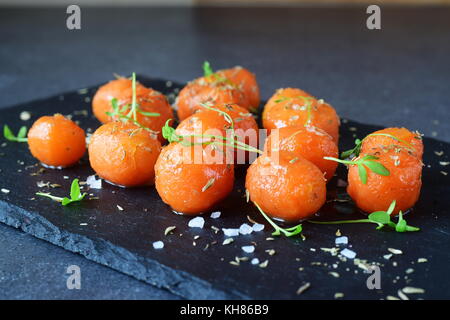 Glassato al miele carotine con sale marino e il timo su un grigio Sfondo astratto. Il mangiare sano concetto. il digiuno cibo. pasto sano Foto Stock