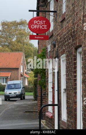 Vista esterna del piccolo villaggio rurale post office shop (chiusa oggi) con casella postale, segno rosso, windows & porta - Bugthorpe, nello Yorkshire, Inghilterra, Regno Unito. Foto Stock