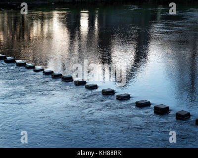 Pietre miliari attraverso il Fiume Wharfe e di riflessione del Priorato rovine al tramonto Bolton Abbey North Yorkshire, Inghilterra Foto Stock