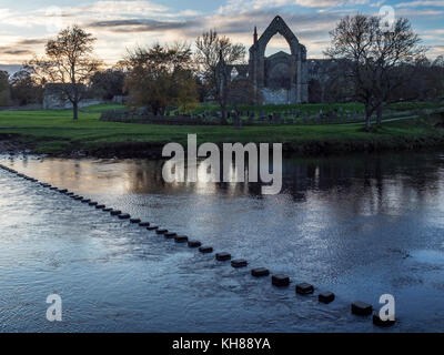 Pietre miliari attraverso il Fiume Wharfe e il Priorato di rovine al tramonto Bolton Abbey North Yorkshire, Inghilterra Foto Stock