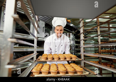 Un uomo baker con un vassoio di tortine. Foto Stock