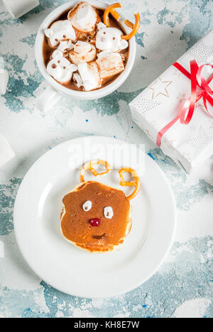 Idea per una per bambini Colazione di natale: frittelle decorato come santa's cervi, cacao con Teddy Bear e cervi marshmallow. su una luce blu backgrou Foto Stock