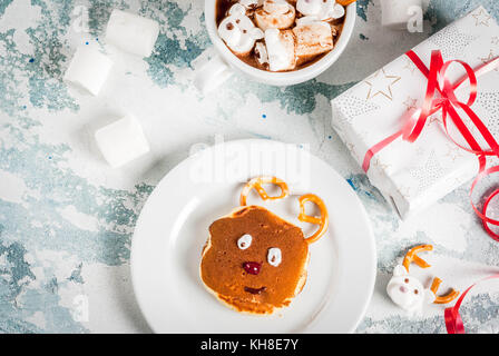 Idea per una per bambini Colazione di natale: frittelle decorato come santa's cervi, cacao con Teddy Bear e cervi marshmallow. su una luce blu backgrou Foto Stock