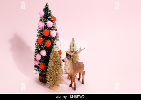 Golden abeti e albero di Natale decorato con pompon con figurine renne accanto ad esso su un vivace colore rosa sfondo. Il minimo ancora vita fotogr Foto Stock