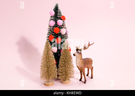 Golden abeti e albero di Natale decorato con pompon con figurine renne accanto ad esso su un vivace colore rosa sfondo. Il minimo ancora vita fotogr Foto Stock