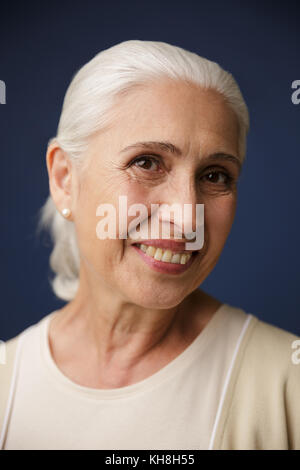 Close-up ritratto di allegro vecchia donna che guarda la fotocamera, su sfondo blu scuro Foto Stock