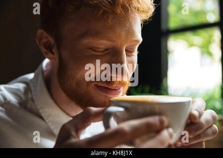 Close-up ritratto di allegro readhead uomo barbuto sniffs caffè con gli occhi chiusi Foto Stock