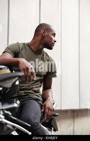 Ritratto di un concentrato di giovani afro american uomo seduto su una motocicletta e guardando lontano all'aperto Foto Stock