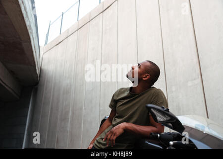 Ritratto di un concentrato di giovani afro american uomo seduto su una motocicletta e cercando fino all'aperto Foto Stock