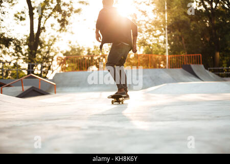 Giovani afro american guidatore di skateboard pattinaggio su un calcestruzzo rampa di skateboard a skate park Foto Stock