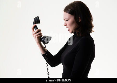 Rottura delle relazioni: Una giovane ragazza caucasica dai capelli castani arrabbiata che grida al telefono, tenendo in mano un ricevitore telefonico Bakelite nero vecchio stile Foto Stock