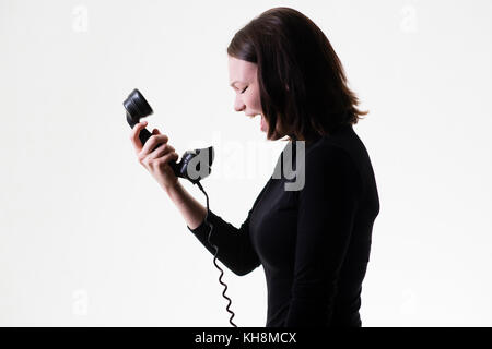 Rottura delle relazioni: Una giovane ragazza caucasica dai capelli castani arrabbiata che grida al telefono, tenendo in mano un ricevitore telefonico Bakelite nero vecchio stile Foto Stock