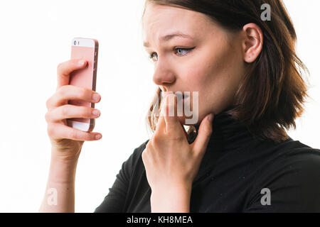 Hacking e cyber bullismo: Una giovane ragazza caucasica dai capelli castani sul suo cellulare , smartphone, cellulare, che sembra preoccupata, confusa, preoccupata, per il contenuto del messaggio che sta vedendo, Regno Unito Foto Stock