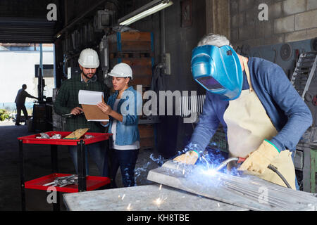 Saldatore lavoratore metalmeccanico utilizzando abbigliamento protettivo in officina di metallurgia Foto Stock