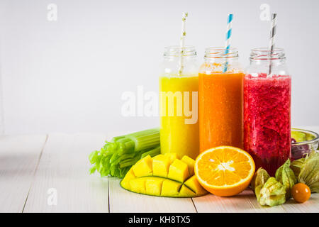 Frullati multicolore in bottiglie di mango, arancio, banana, sedano, bacche, su di un tavolo di legno Foto Stock