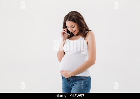 Immagine di sorridente donna incinta isolate su sfondo bianco parla al telefono cellulare. Guardando a parte. Foto Stock