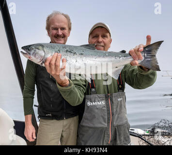 Due uomini in barca da pesca, con un salmone catturato, nebbiosa mattina nello stretto di Johnstone fuori dall'isola di Vancouver, British Columbia, Canada Foto Stock