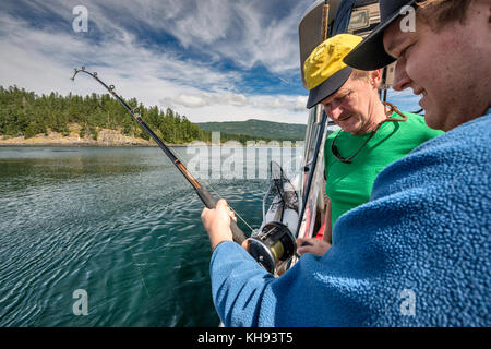 Due uomini, padre e figlio, con canna da pesca, su una barca da pesca nello stretto di Johnstone al largo dell'isola di Vancouver, British Columbia, Canada Foto Stock