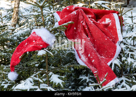 Il santa claus costume si blocca su abete rosso in inverno foresta. deserte santa claus vestiti in boschi innevati. Foto Stock