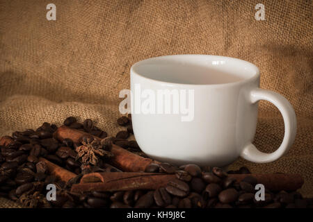 I chicchi di caffè e la tazza di caffè sul tessuto sacco selezionare focus, vintage tono di colore o tonalità scura Foto Stock