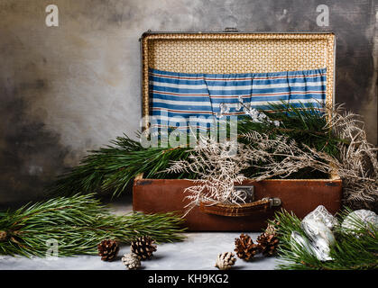 Verde scuro dei rami d abete marrone con coni e albero di natale giocattoli in un marrone retrò valigia con un blu e bianco delle tasche su un grigio con un divorzio indietro Foto Stock