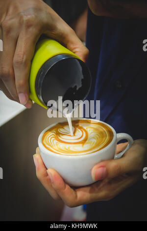 Barista versando il latte dal lanciatore per una tazza di caffè latte art Foto Stock