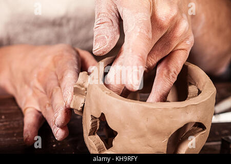 Close-up di una donna potter scolpisce una argilla marrone candeliere e rende il foro a forma di stelle di luce sullo sfondo di un tavolo di legno nel Foto Stock