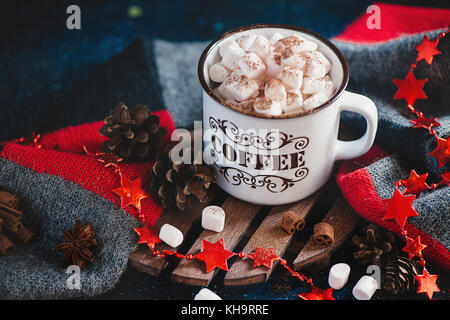 Natale cioccolata calda con marshmallows, cannella, sciarpa lavorata a maglia, stelle, pigne e festoni su un caldo sullo sfondo di legno Foto Stock